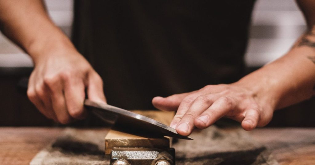 Person carefully sharpening a kitchen knife on a fixed abrasive stone