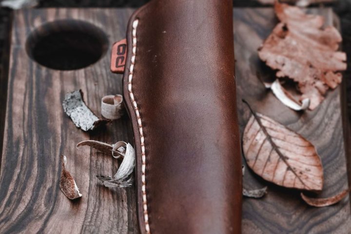 Outdoor knife secured in a stitched leather sheath on a wooden board