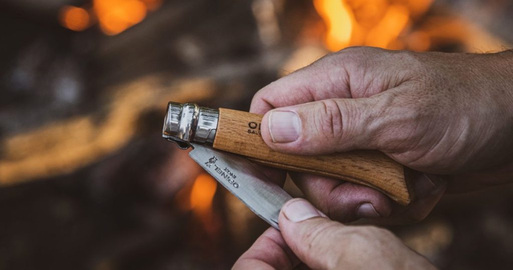 Hands opening a compact folding pocket knife beside a campfire