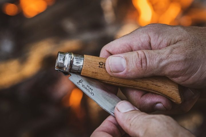 Hands opening a compact folding pocket knife beside a campfire